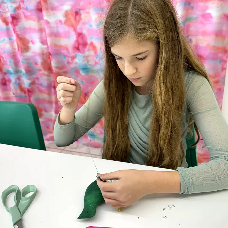 Young child hand-sewing a felt project at beginner summer sewing camp